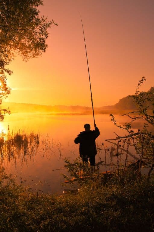 pêcheur avec sa canne à pêche au coucher du soleil